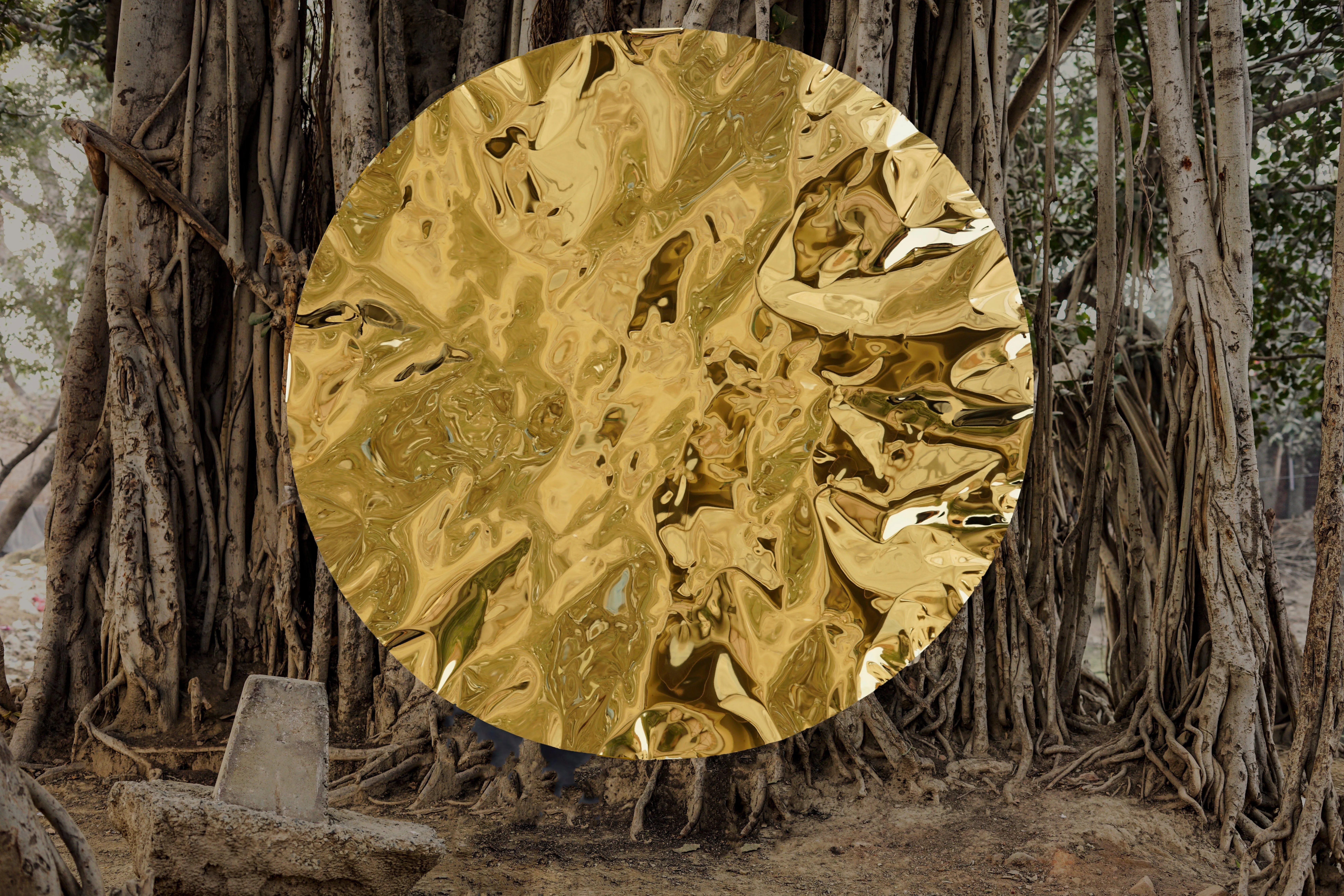 A crumpled gold mirror disc suspended before a banyan tree, work by Hussain Jamil